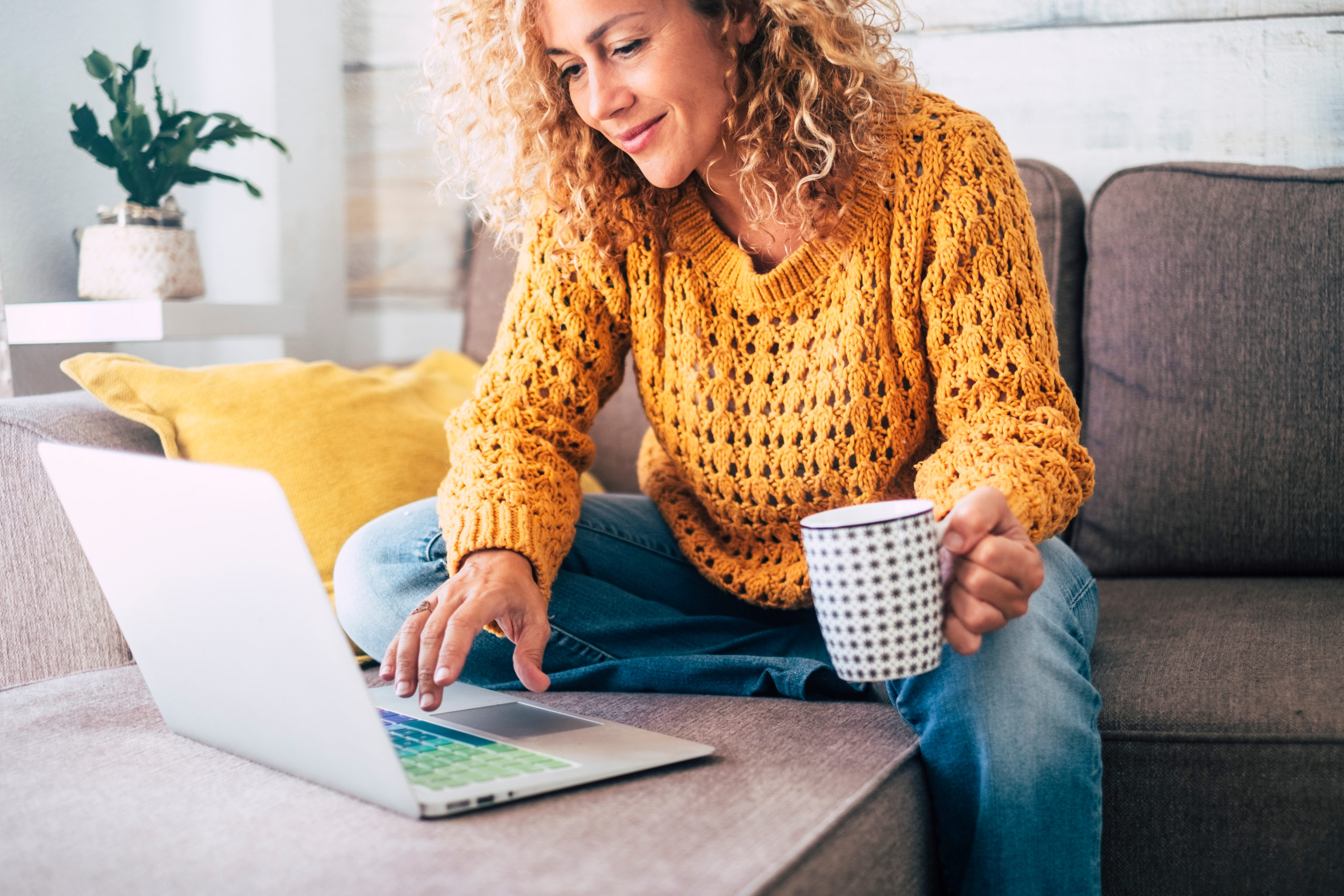 Women in fall sweater on laptop in home with tea