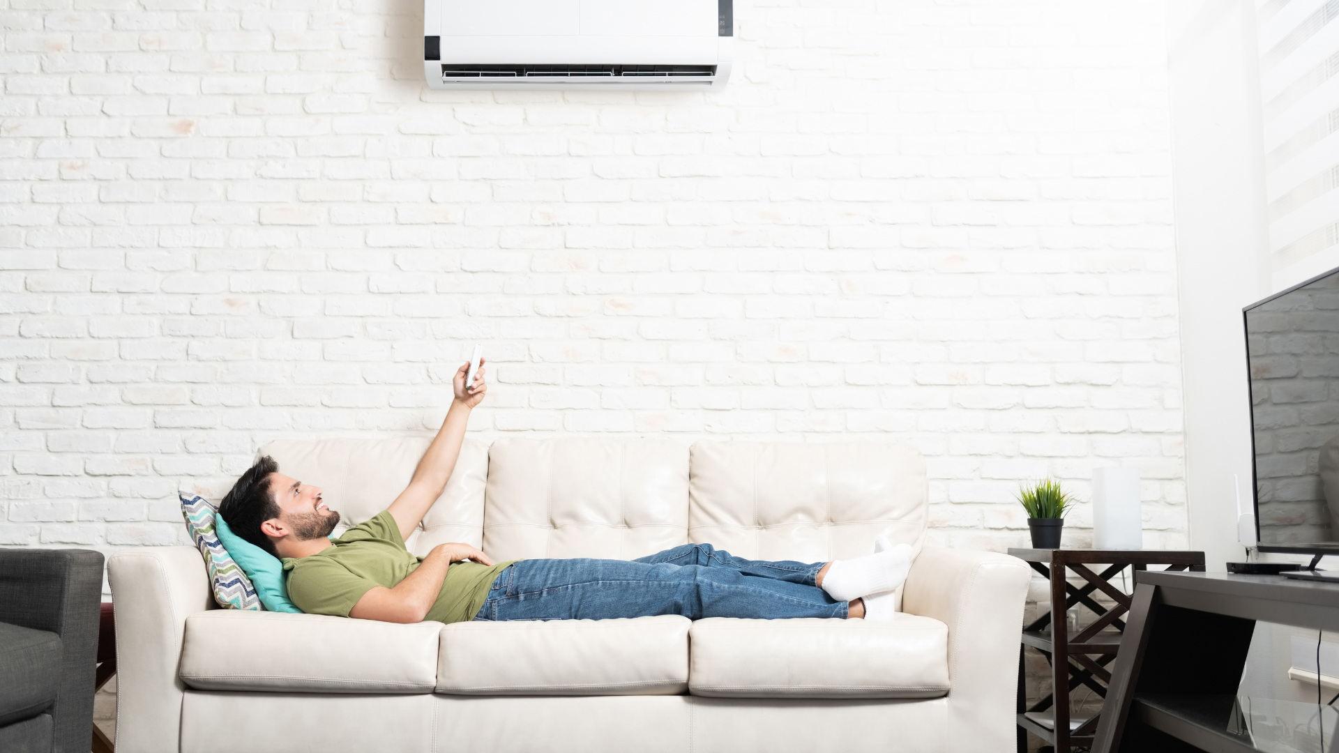 man laying on a couch turning on heat pump with wireless remote