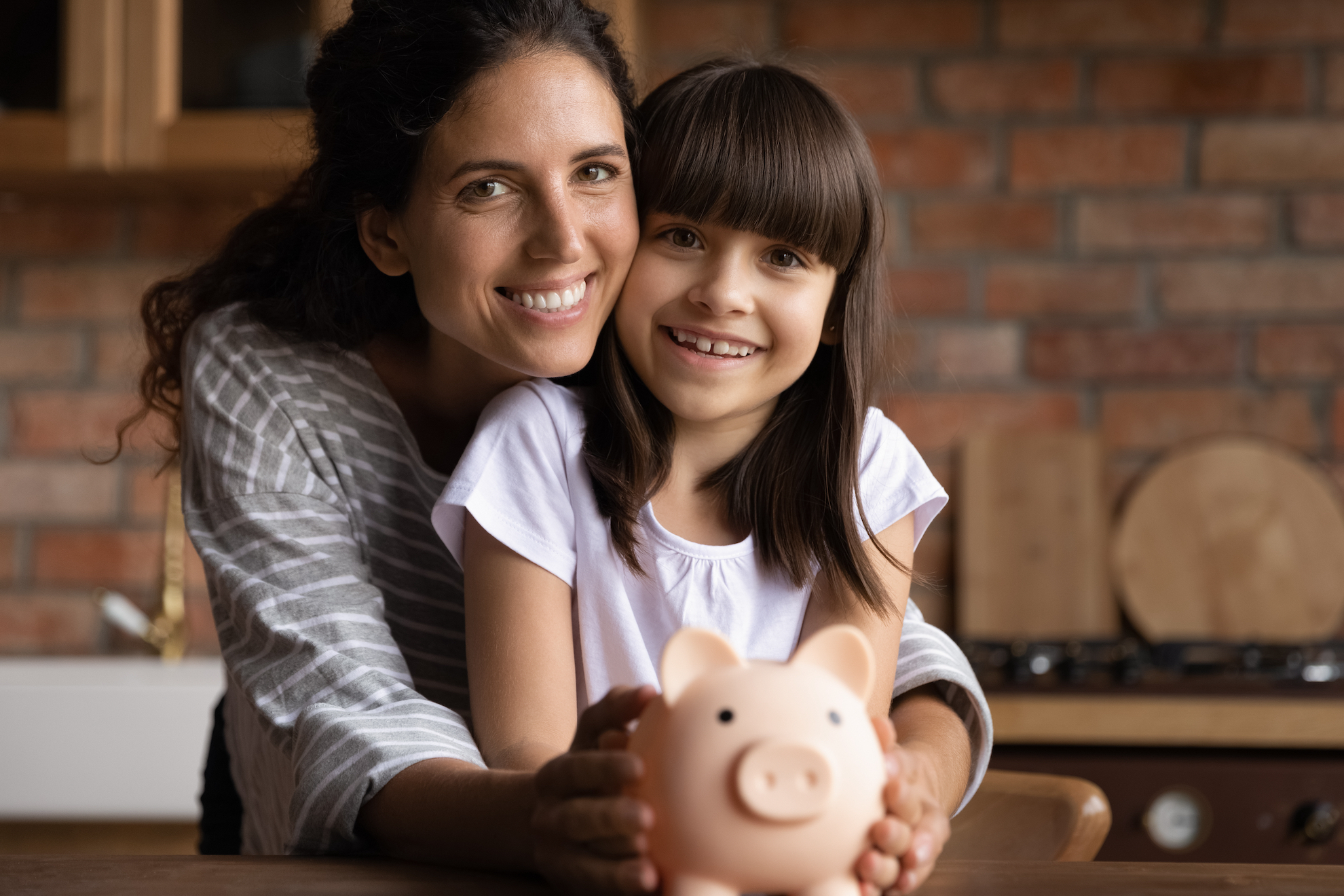 happy mother and daughter holding a piggy bank in kitchen