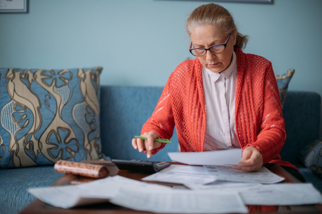 An elderly woman is sitting at a table with documents, counting the costs of energy bills.
