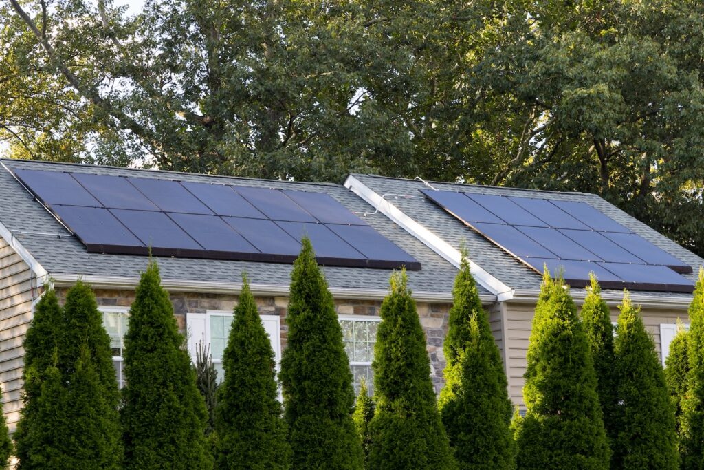 Solar panels installed on residential home in New England with trees in background and small manicured trees out front