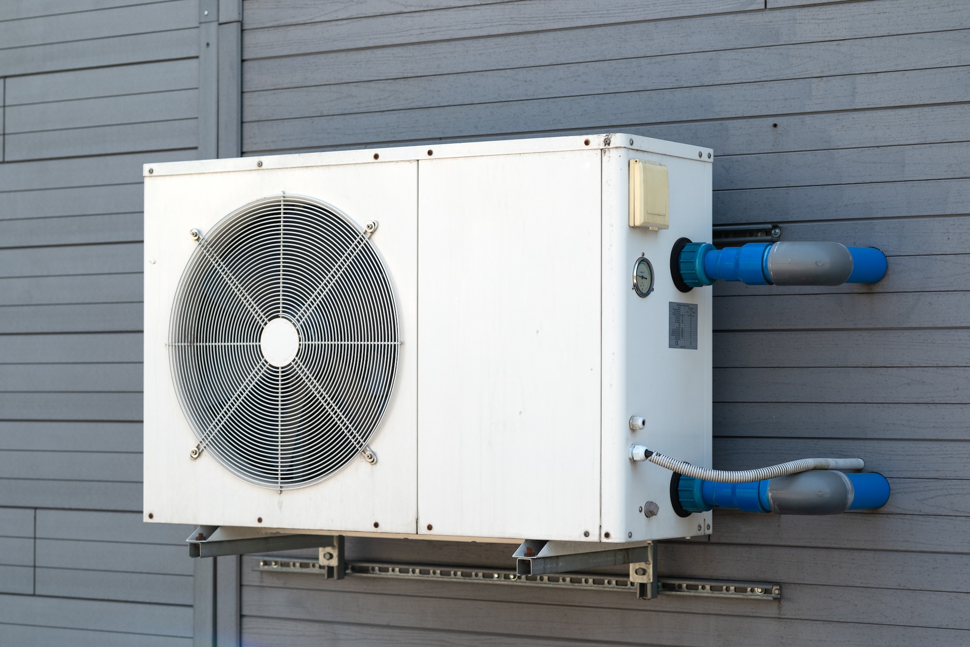 Condensing unit of heat pump system on exterior of blue grey home