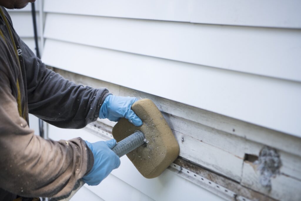 Neeeco insulation technician insulating existing exterior walls of white home in Massachusetts