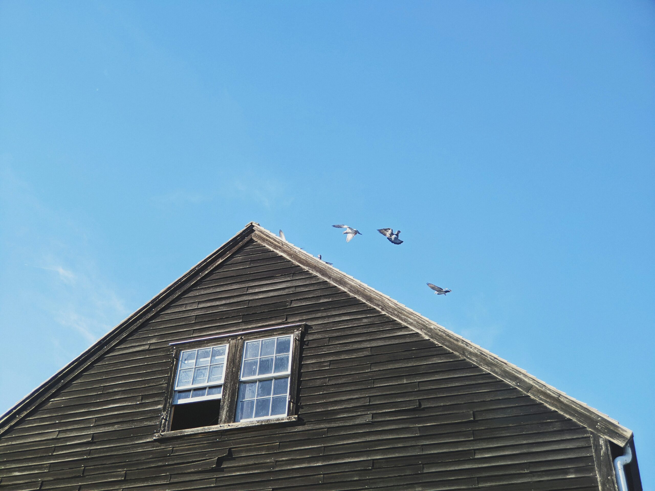 Massachusetts home with two windows near peak of roof. One window is opened halfway.