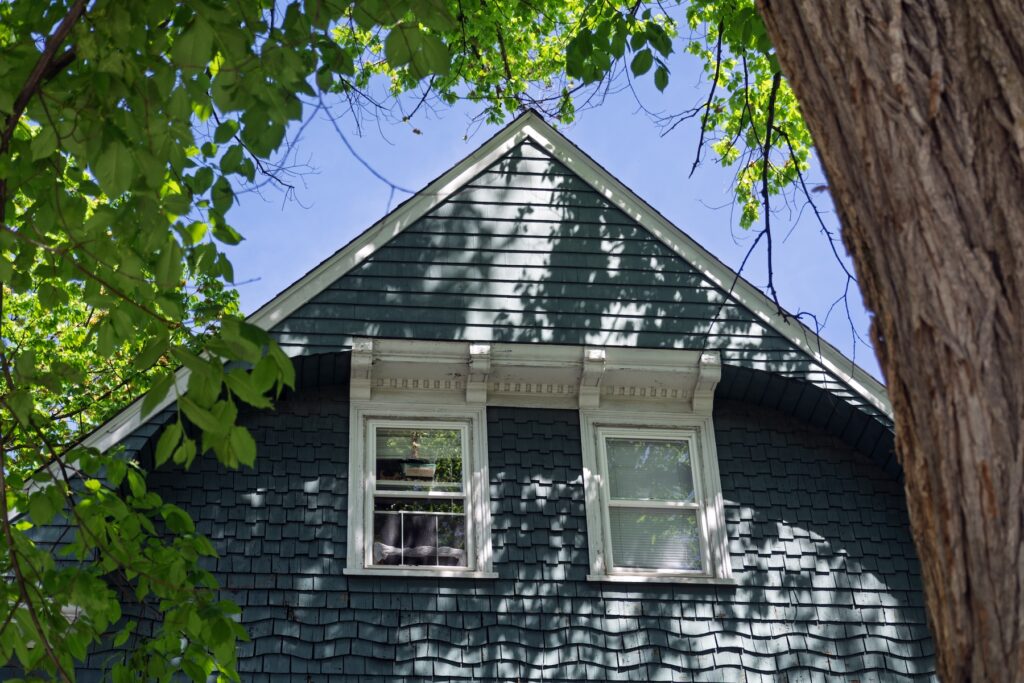 Two upper windows with ornate white decorative trim on a classic house framed by green summer foliage in Boston